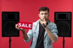 Man holding a sale sign next to a speaker, making a shushing gesture, representing the concept of sell beats online
