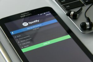 Smartphone displaying Spotify login screen next to a laptop and earphones on a desk, representing how to get on Spotify and grow as an artist